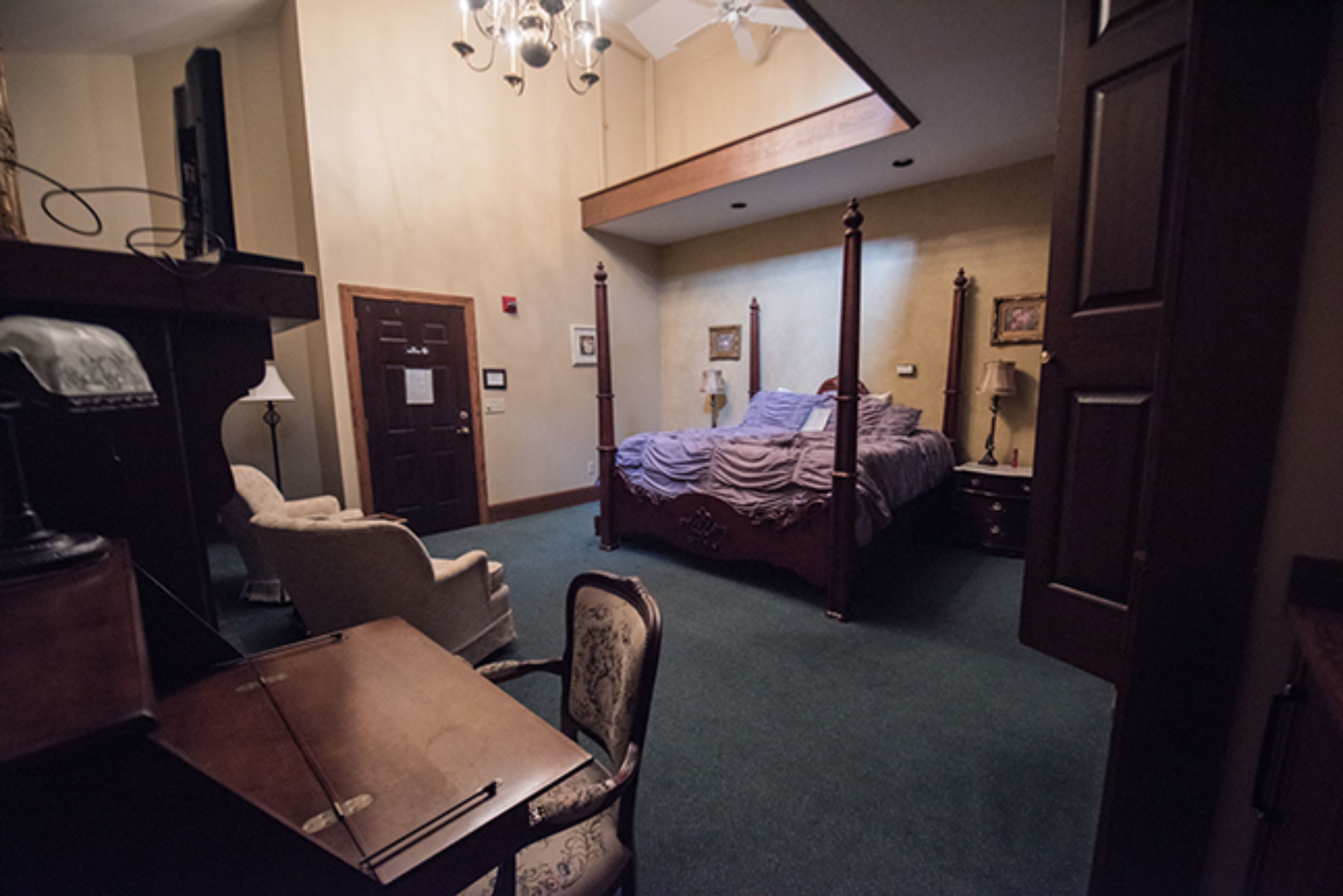 A bedroom with a four-poster bed, a desk, a chair, and a wardrobe.