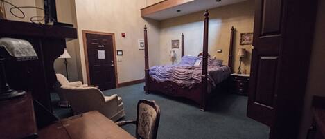 A bedroom with a four-poster bed, a desk, a chair, and a wardrobe.