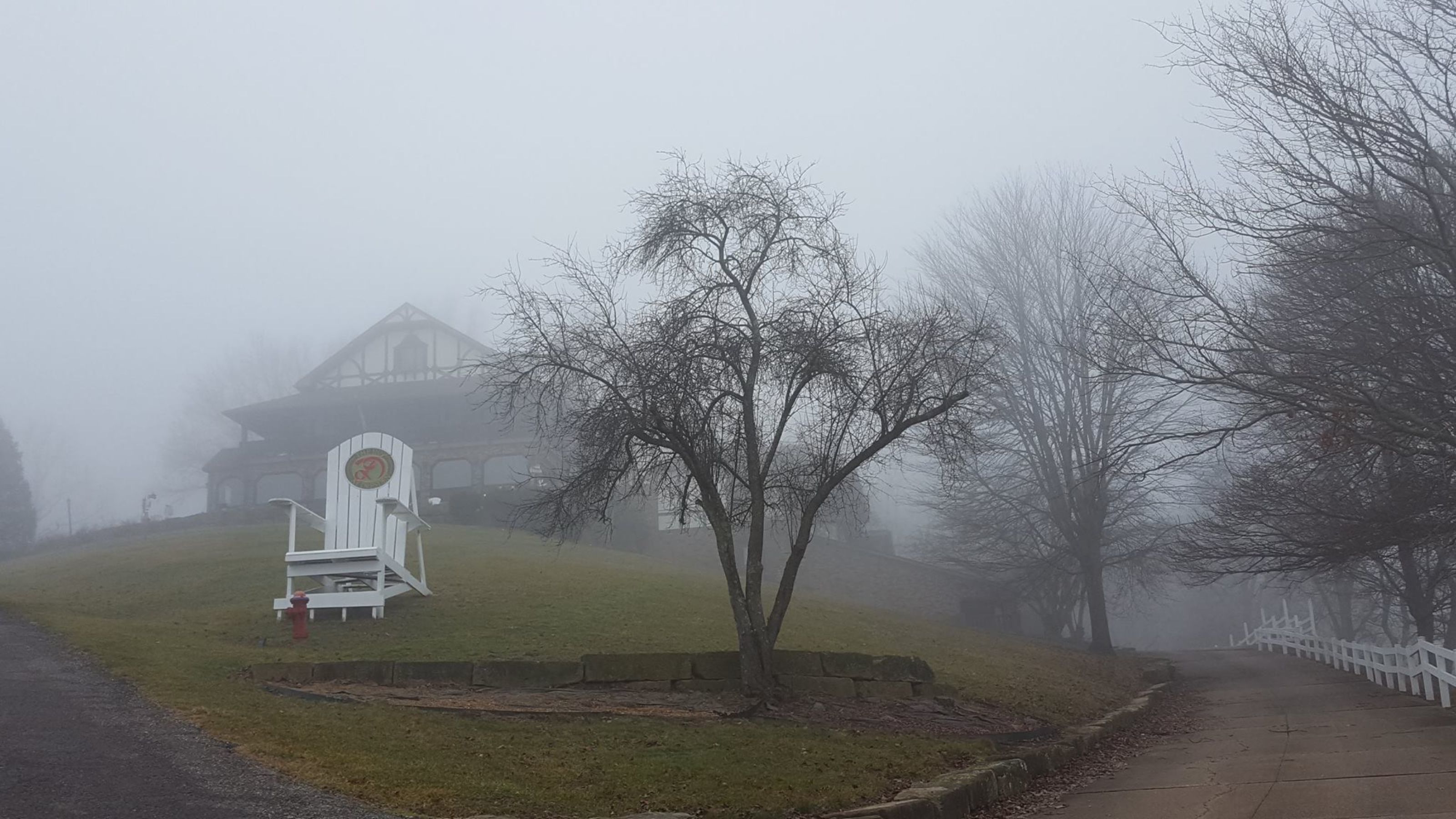 Un paysage brumeux avec un bâtiment blanc, un banc et un arbre.