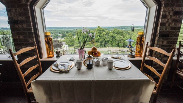 A dining table set for two with a view of a green landscape through a large window. - The Inn at Dresden (Dresden)