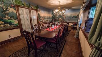 Uma sala de jantar com uma longa mesa de madeira, cadeiras estofadas vermelhas e um candelabro.