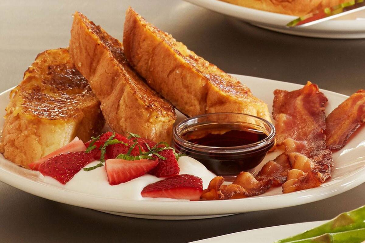 A plate with French toast, strawberries, bacon, and syrup.