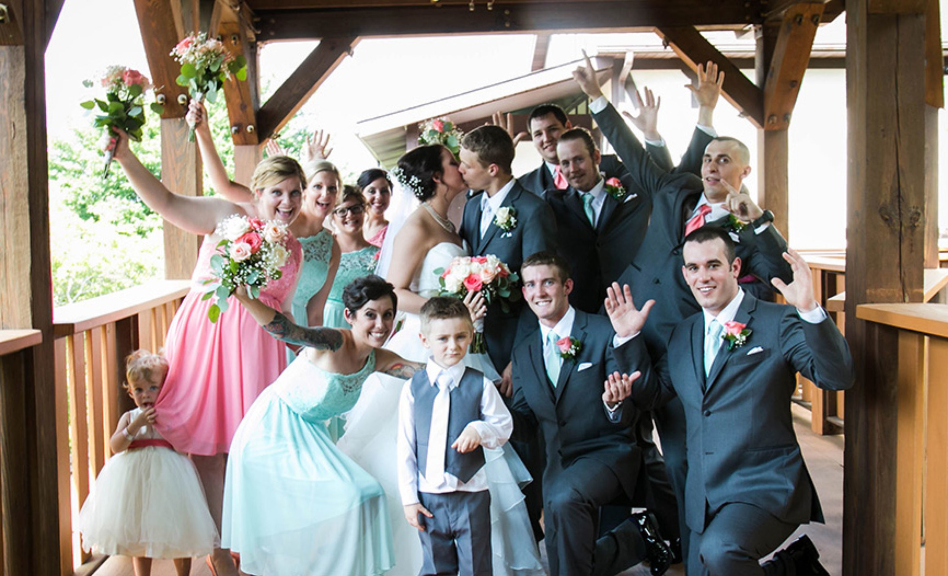 Eine Gruppe von Personen in festlicher Kleidung, vermutlich bei einer Hochzeit, unter einer Holzkonstruktion mit Blick auf eine grüne Landschaft.