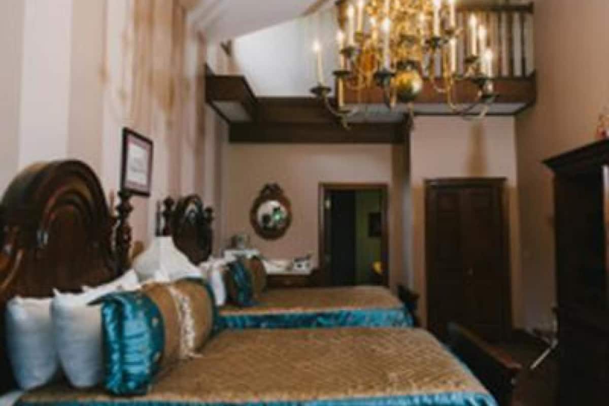 A traditional bedroom with two beds, a chandelier, and a wooden wardrobe.