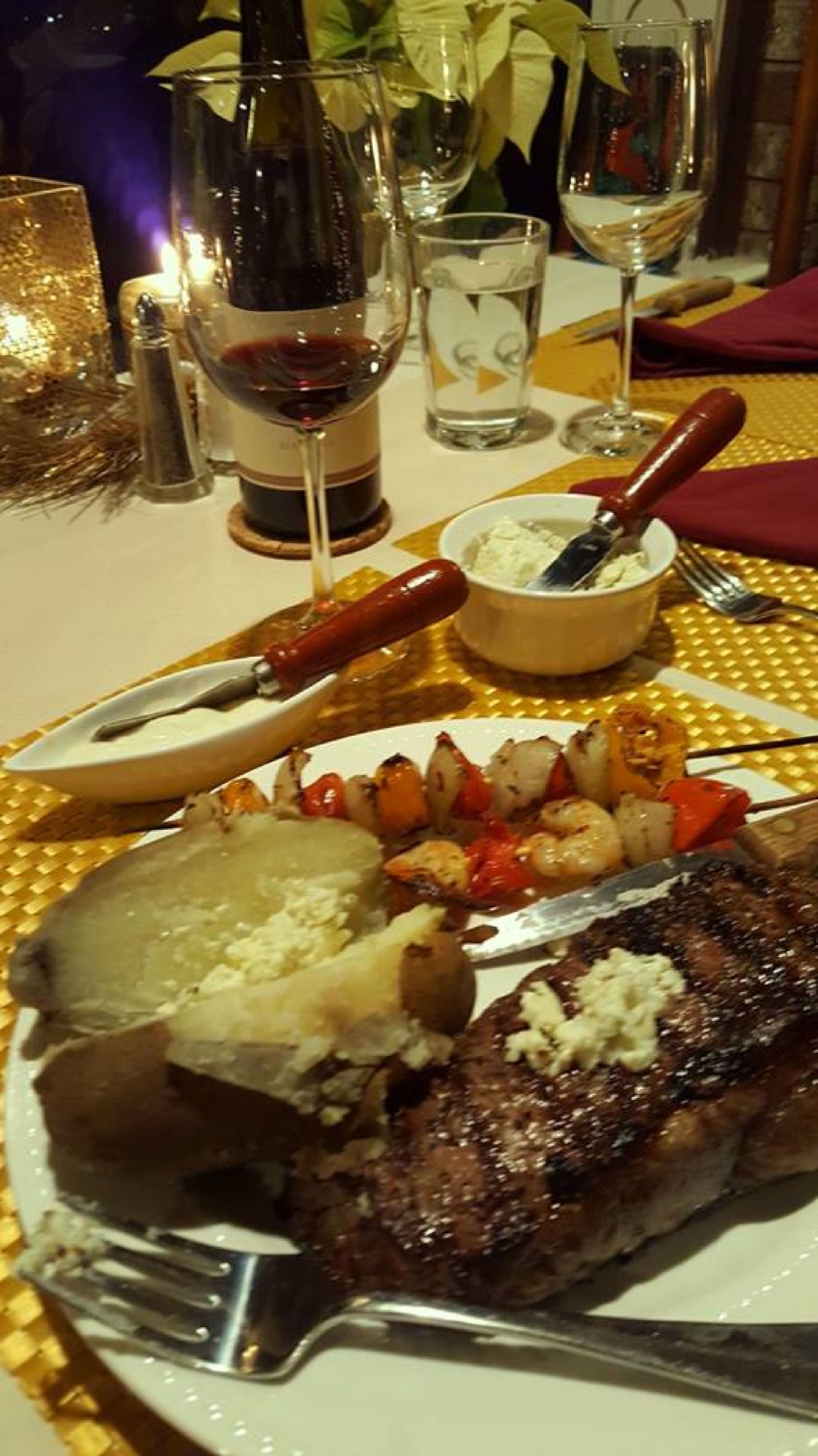 Una mesa de comedor con un bistec, verduras a la parrilla y un bol de salsa.