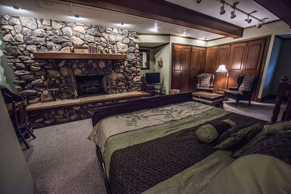 A bedroom with a stone fireplace, a large bed, a chair, and a desk.