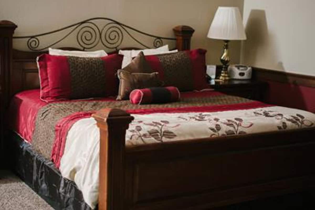 A neatly made bed with a floral bedspread and multiple pillows, a bedside lamp, and a wooden headboard.