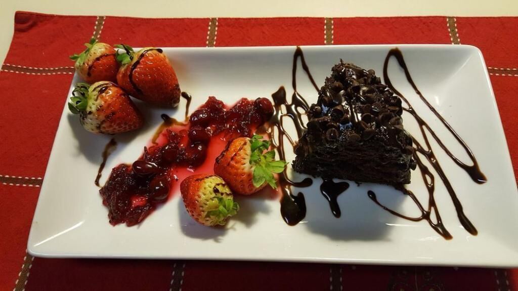Ein weißer Teller mit Erdbeeren, einem Schokoladendessert und einer Beerensoße auf einer roten Tischdecke.