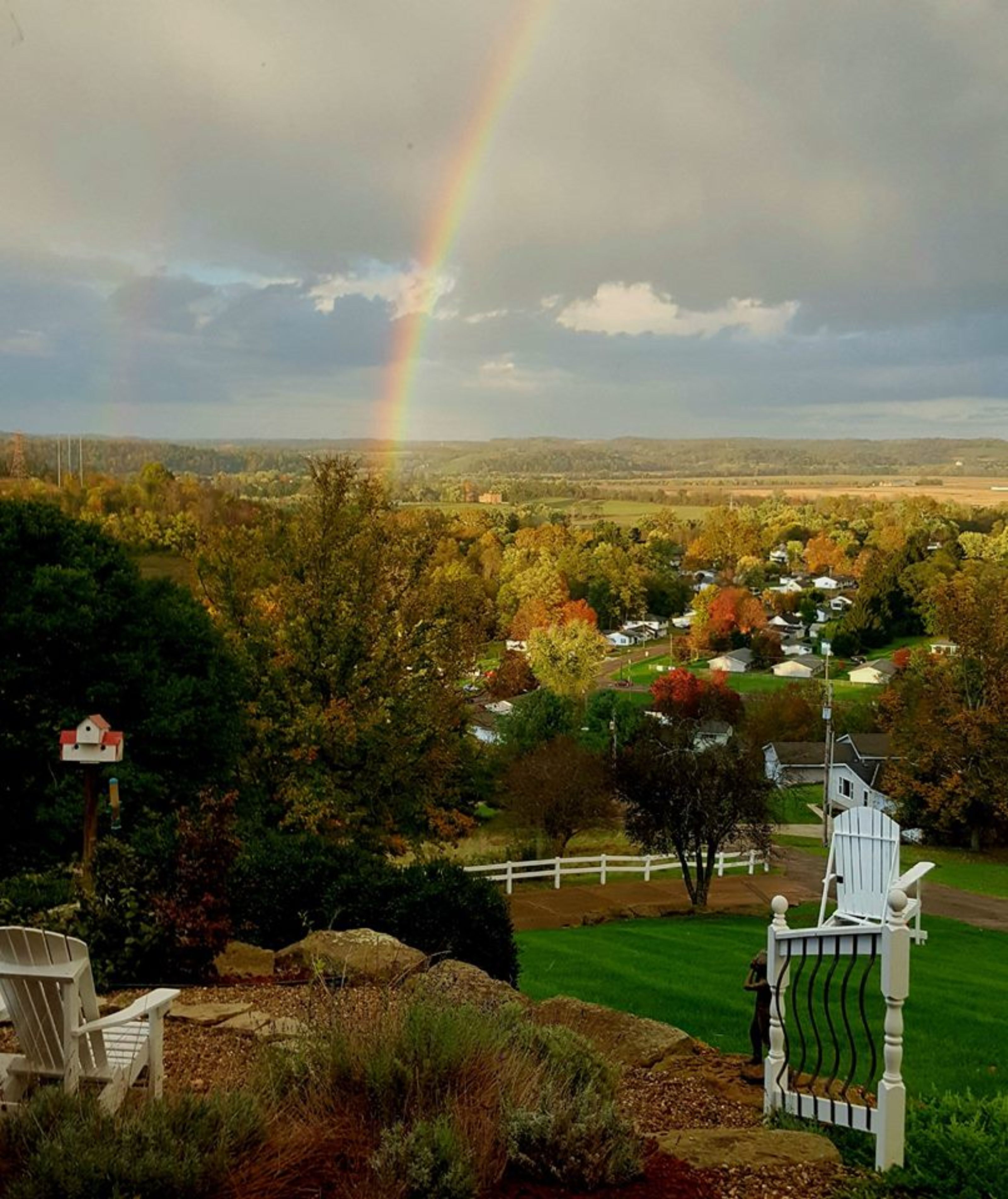 A rural landscape with a rainbow, houses, and a white gate.