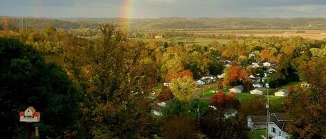 A rural landscape with a rainbow, houses, and a white gate.