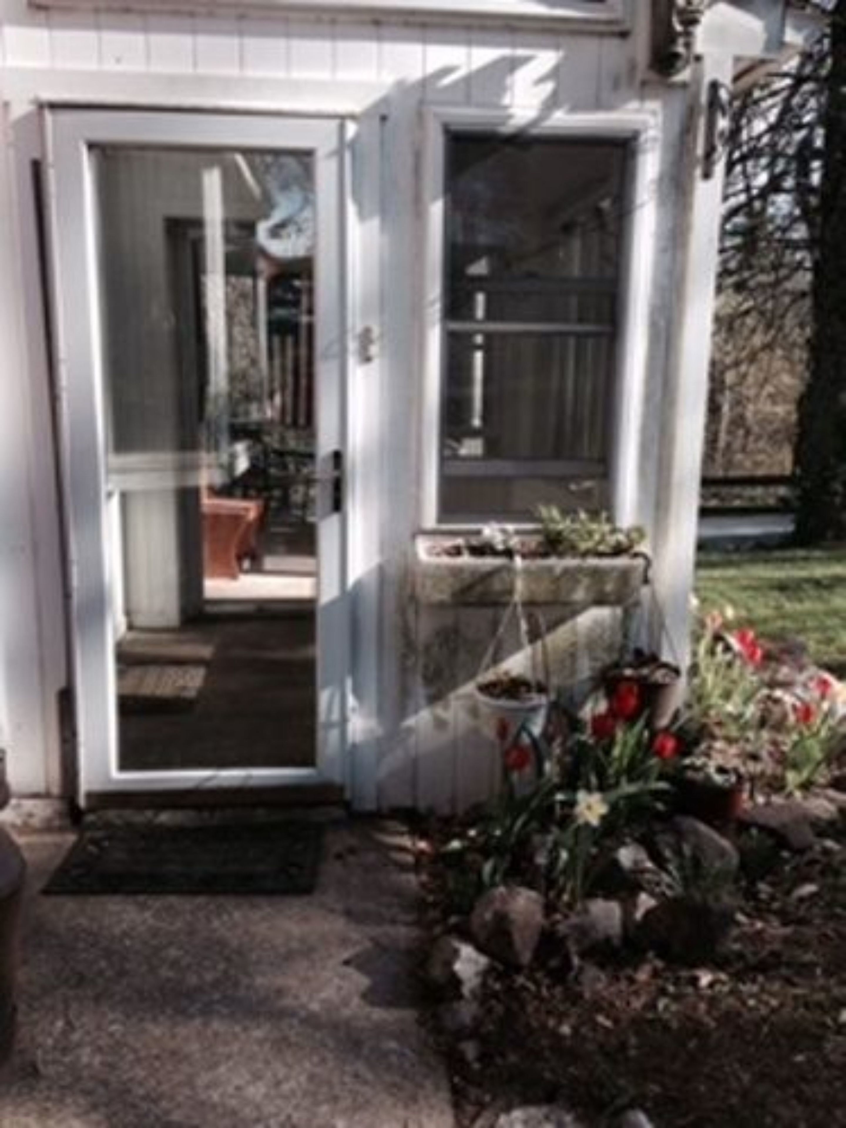 A house with a white exterior, a front door, and a small garden with flowers and rocks.