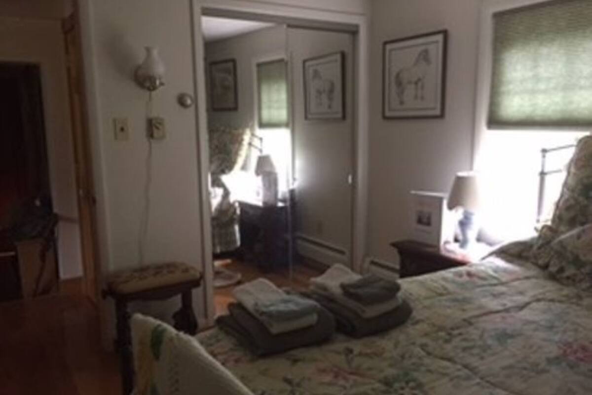 A bedroom with a bed, a chair, a small table, and a mirror.