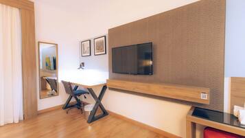 A hotel room with a wooden desk, a chair, a television mounted on the wall, and a mirror.