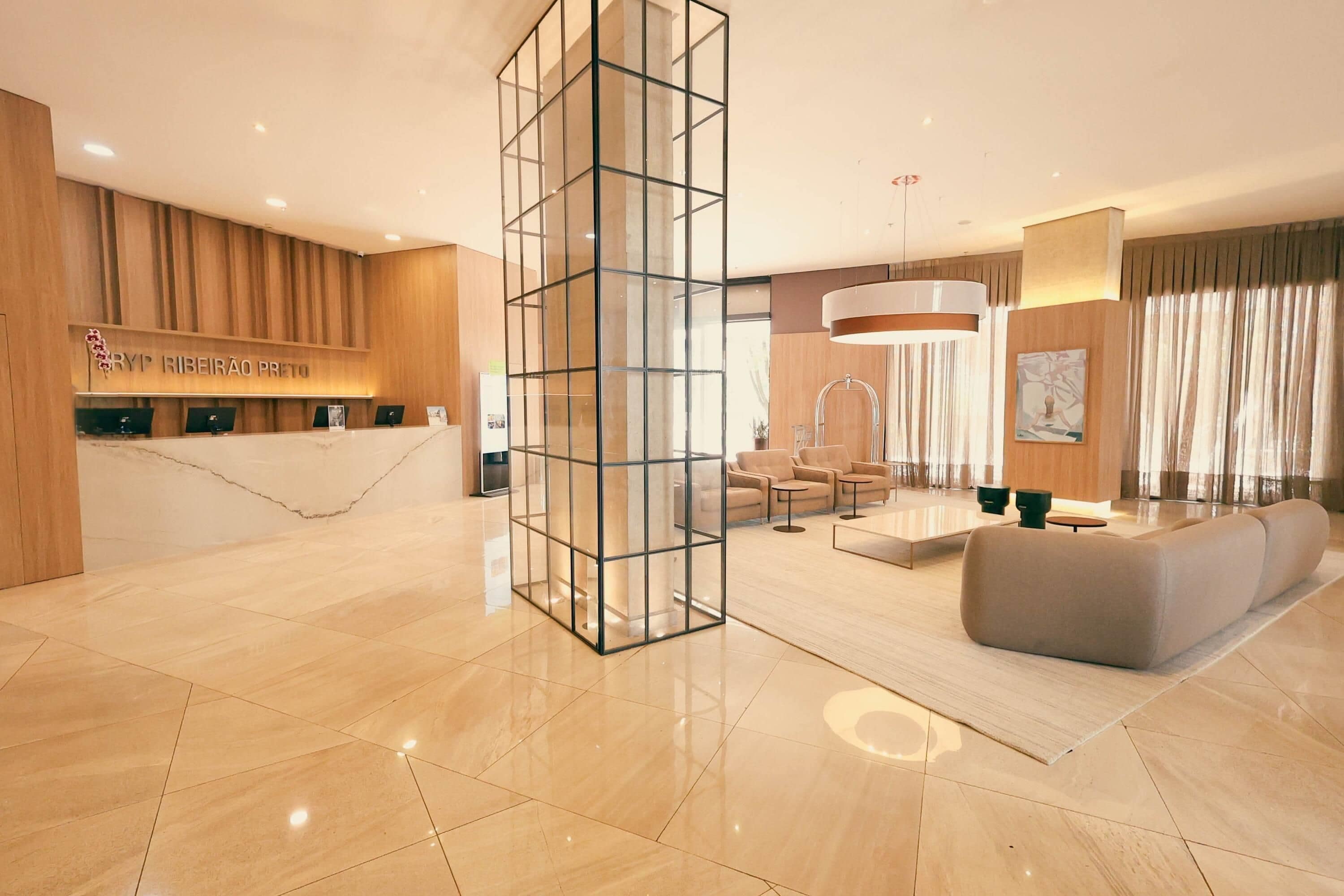 A modern hotel lobby with a reception desk, seating area, and a large glass partition.