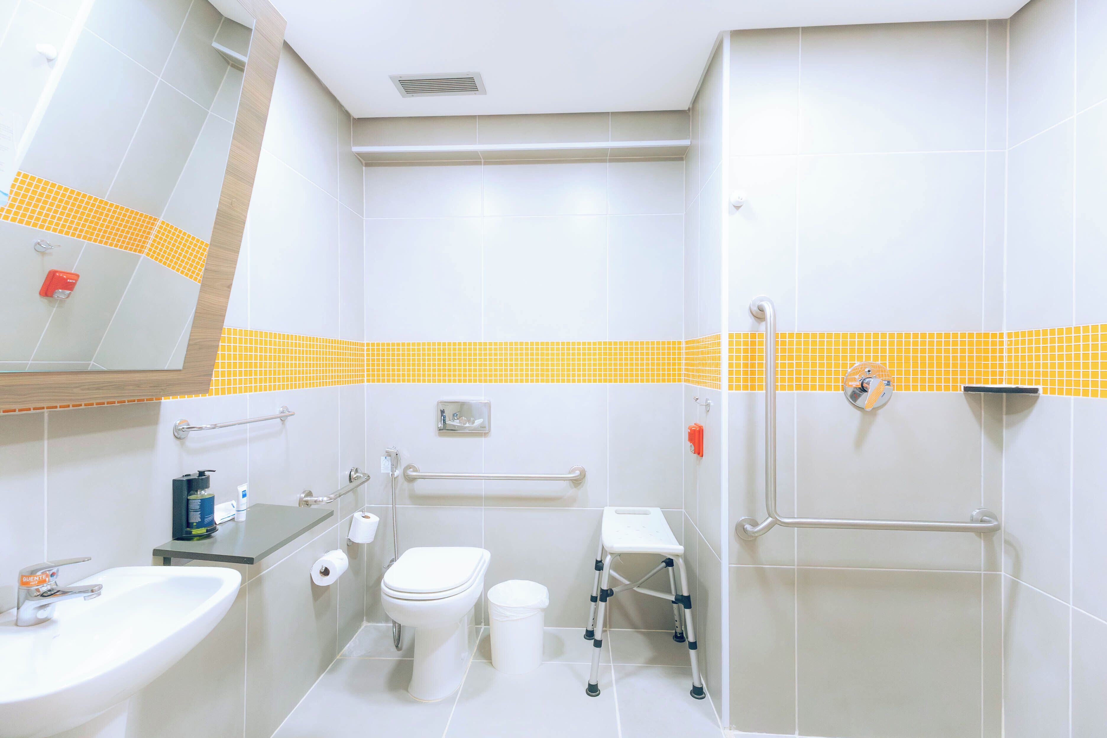 A modern bathroom with a sink, toilet, and shower area. It includes grab bars and a wheelchair-accessible bench.