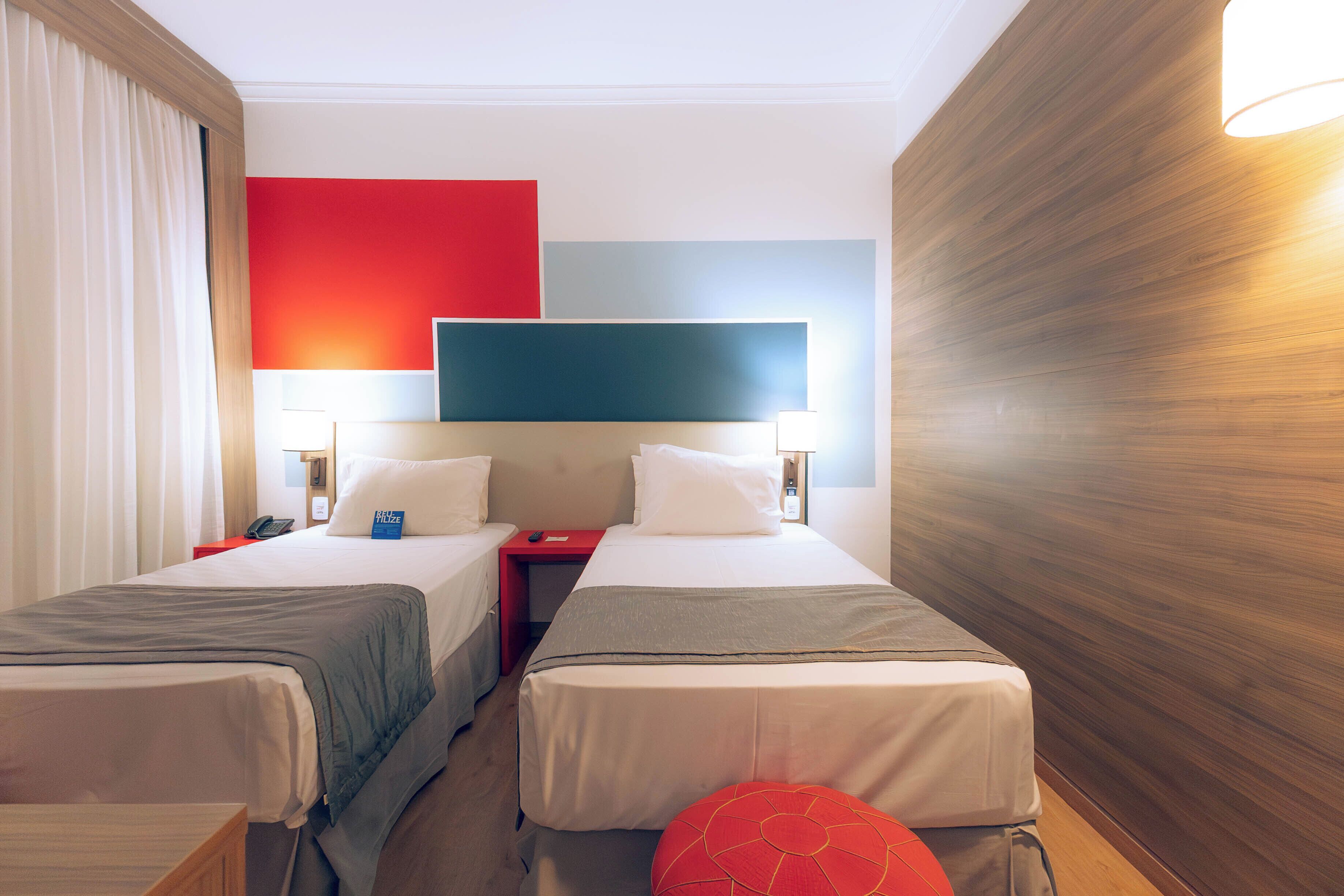 A hotel room with two beds, a TV, and a red accent wall.