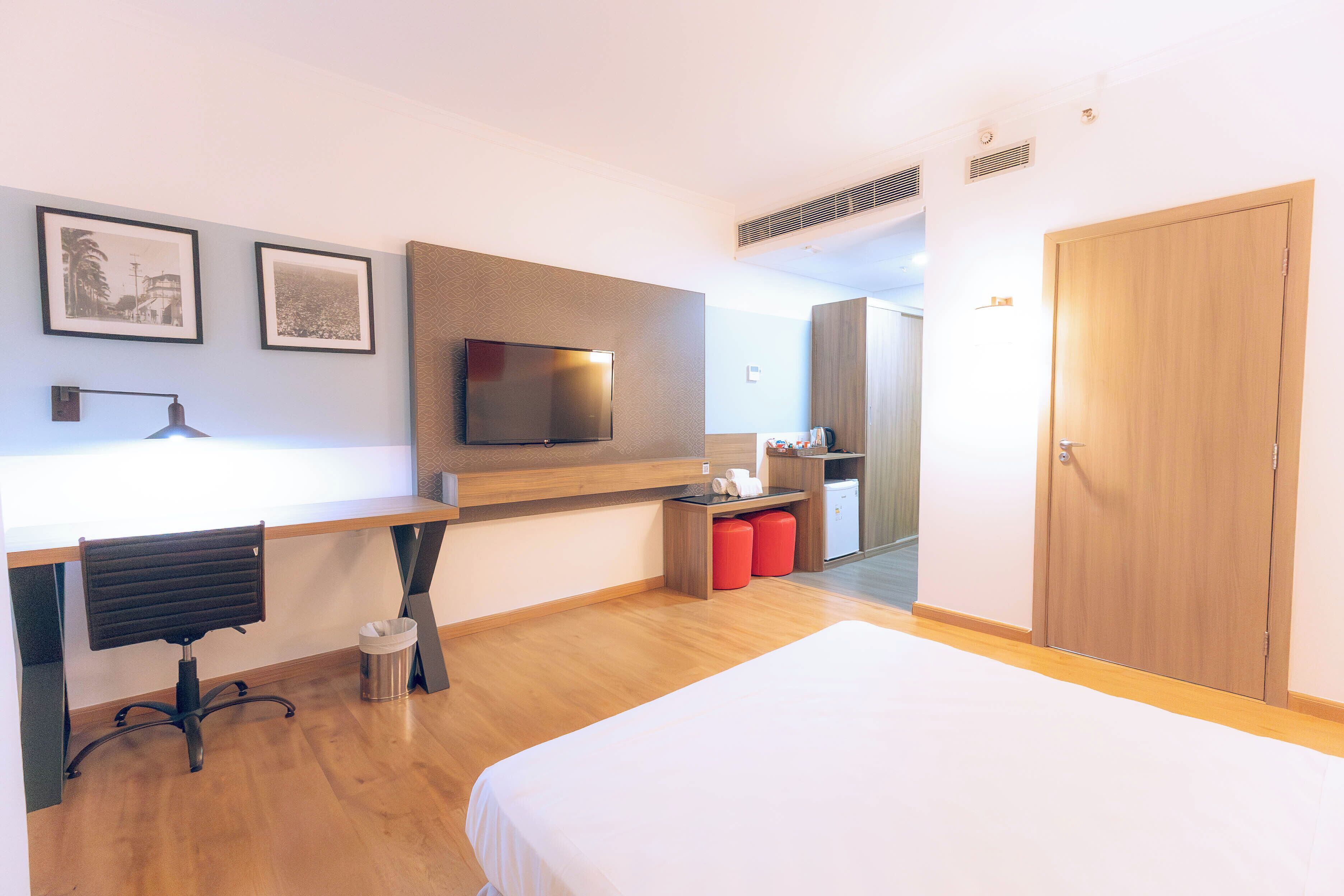 A hotel room with a bed, a desk with a chair, a television, and a wardrobe.