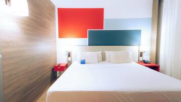 A hotel room with a large bed, a red nightstand, a blue pillow, and a red pillow.