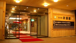 L’entrée d’un hôtel, avec une façade en bois, un tapis rouge et une enseigne portant un texte en japonais.