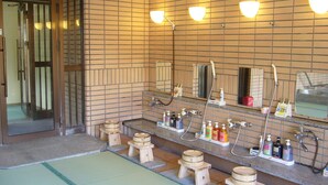 Une salle de bain de style japonais traditionnel, avec des tabourets en bois, un grand miroir et divers produits de toilette disposés sur le comptoir.