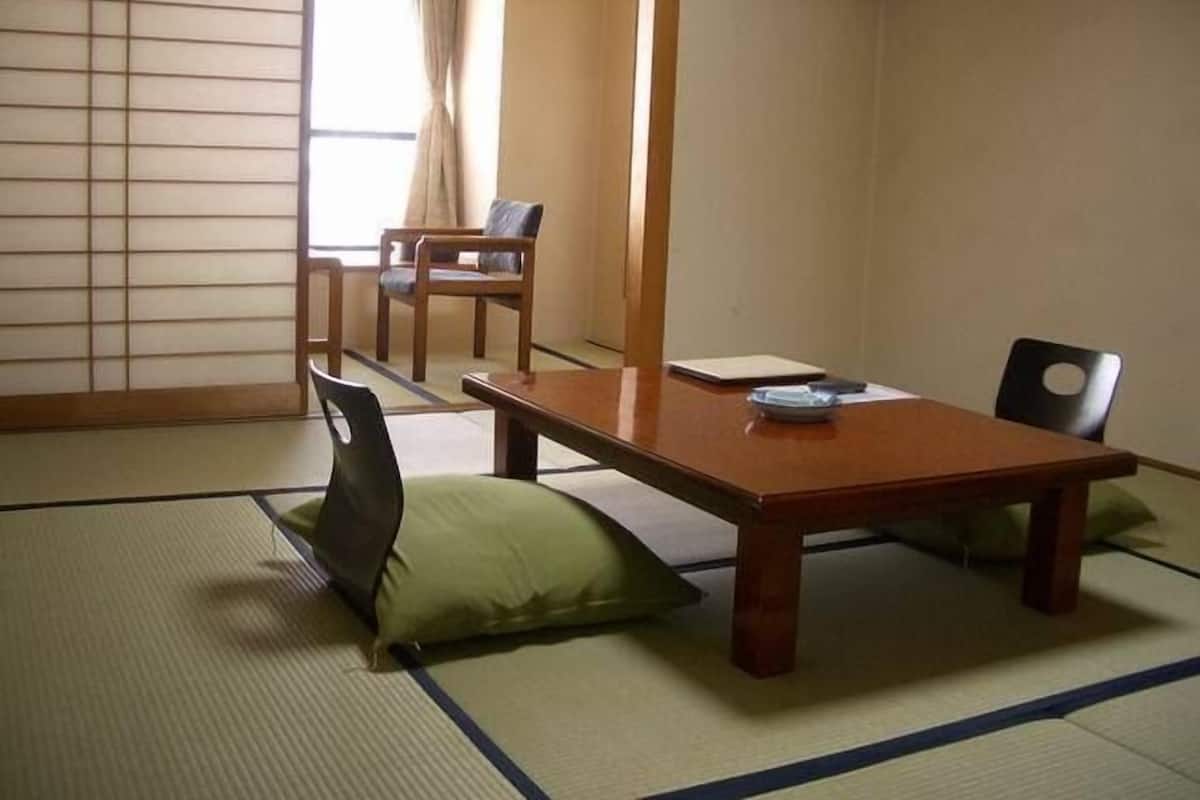 Une pièce de style japonais traditionnel, avec un sol recouvert de tatamis, une petite table en bois, deux chaises et un futon servant de lit.