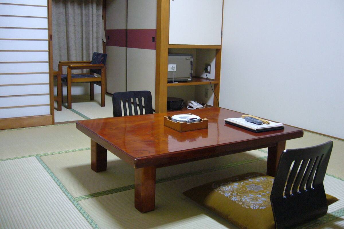 Une pièce de style japonais traditionnel, avec un sol recouvert de tatamis, une table à manger en bois, une chaise noire, une petite étagère avec un téléphone et une porte coulissante.