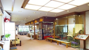 Un hall d’entrée spacieux avec un plafond haut, un comptoir d’accueil, un espace détente et une vitrine contenant des documents d’information.