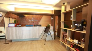 Taulell de recepció d'hotel amb un fons de fusta, un ordinador i una planta.