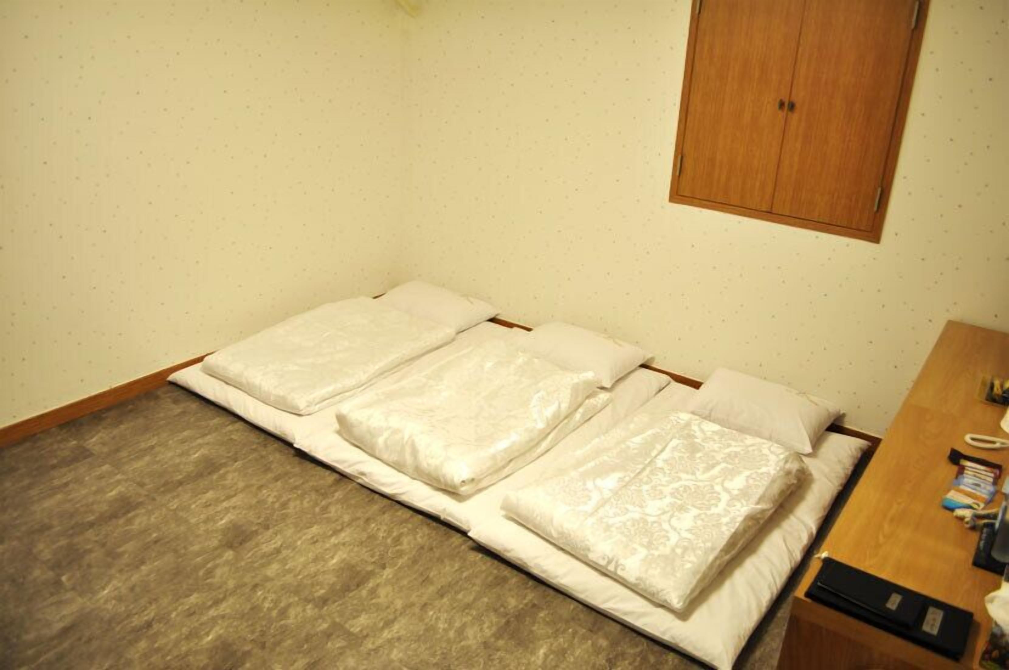 Una habitación pequeña con una cama individual, cabecera de madera, un escritorio de madera con teléfono y un mueble bajo.