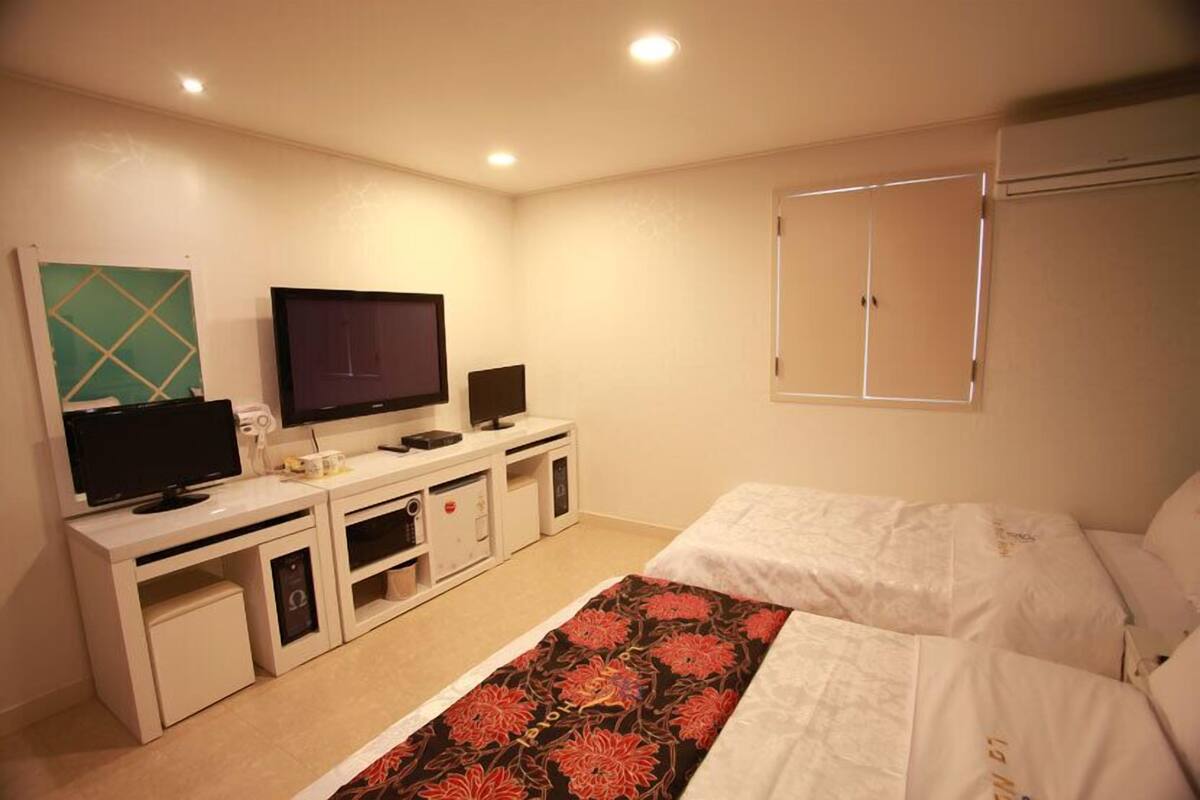 A hotel room with a bed, a TV, a desk with a computer, and a wardrobe.