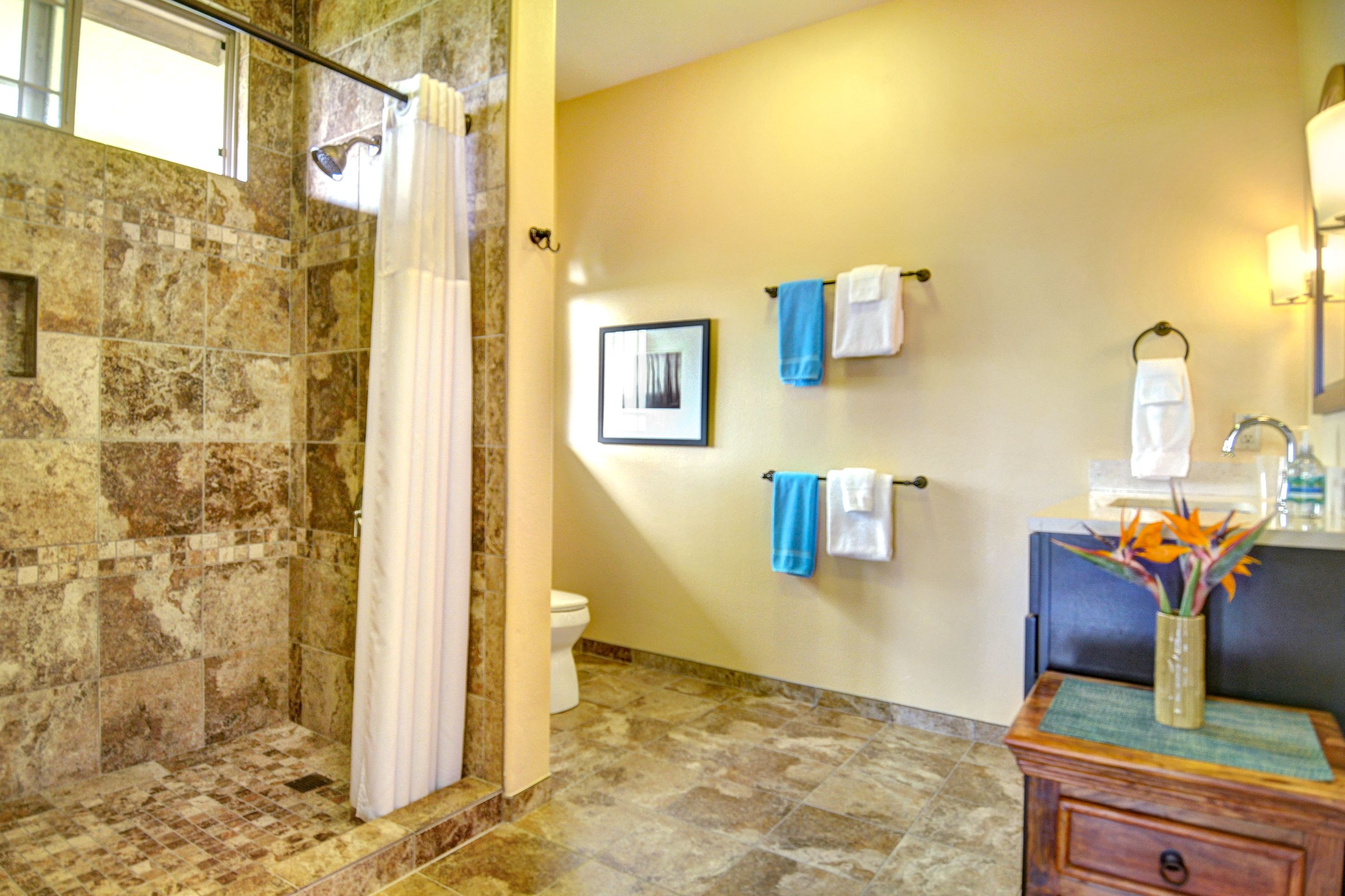 A bathroom with a shower, toilet, and vanity with a vase of flowers.