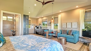 A modern bedroom with a large bed, a kitchenette, a dining area, and a living room with a sofa and TV. - Mahana House Country Inn (Hakalau)
