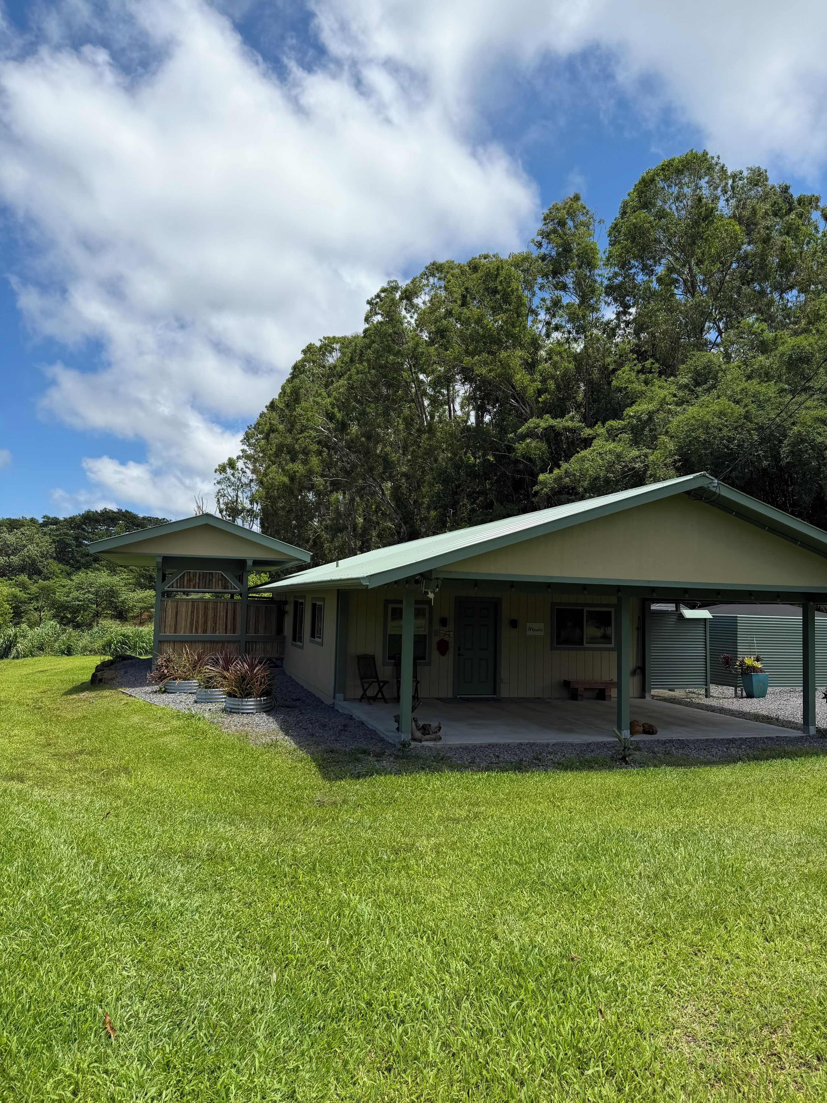 A single-story house with a covered porch, a fenced yard, and a large tree in the background.