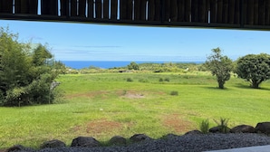A view from a covered area to a grassy field with trees and a distant view of the ocean. - Mahana House Country Inn (Hakalau)