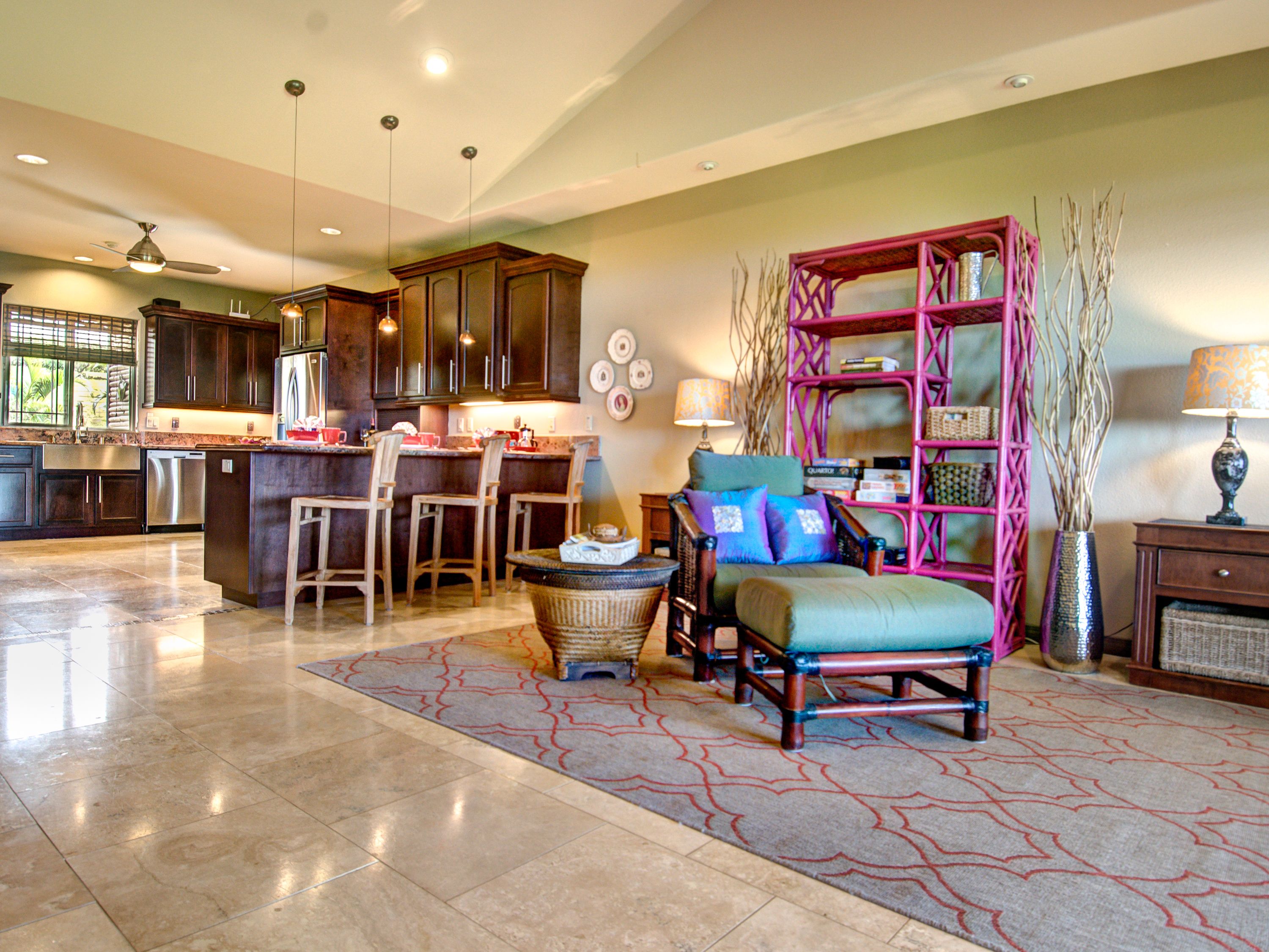 Amplia sala de estar con una cocina al fondo, una zona de estar con una mesa de centro y una estantería decorativa.
