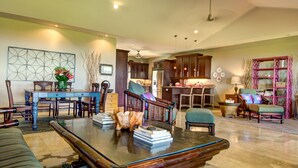 A spacious living area with a dining table, chairs, a coffee table, and a kitchen in the background. - Mahana House Country Inn (Hakalau)