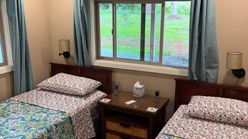 A room with two beds, a window with curtains, a bedside table with a lamp, and a ceiling fan.
