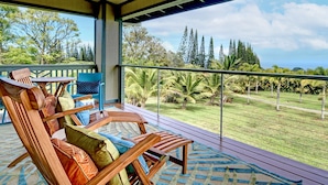 A covered outdoor seating area with wooden chairs and a view of a landscaped garden and trees. - Mahana House Country Inn (Hakalau)