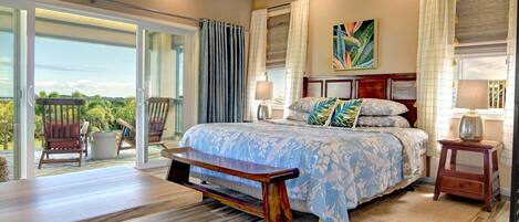 A bedroom with a large bed, a bench, a nightstand, and a view of the outdoors.