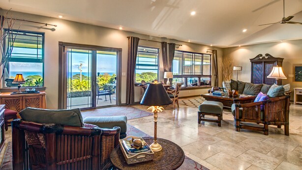 A spacious living area with a large window, a sofa, a coffee table, and a lamp. - Mahana House Country Inn (Hakalau)