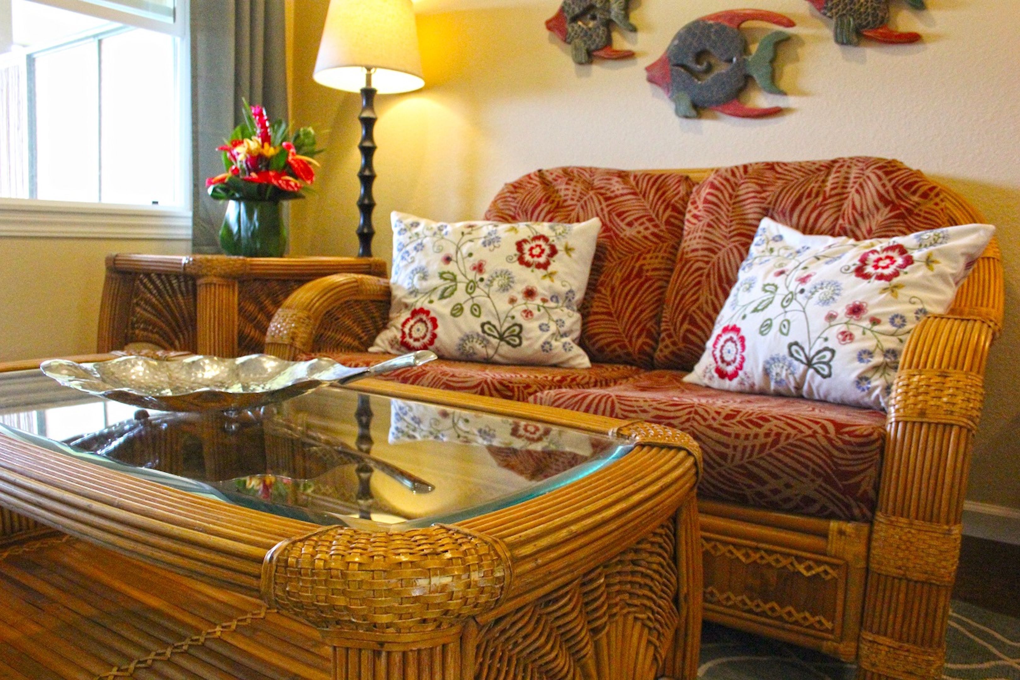A wicker sofa with floral cushions, a glass coffee table, and a lamp.