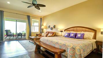 A spacious bedroom with a large bed, a ceiling fan, a bench, and a view of the outdoors through a sliding door.