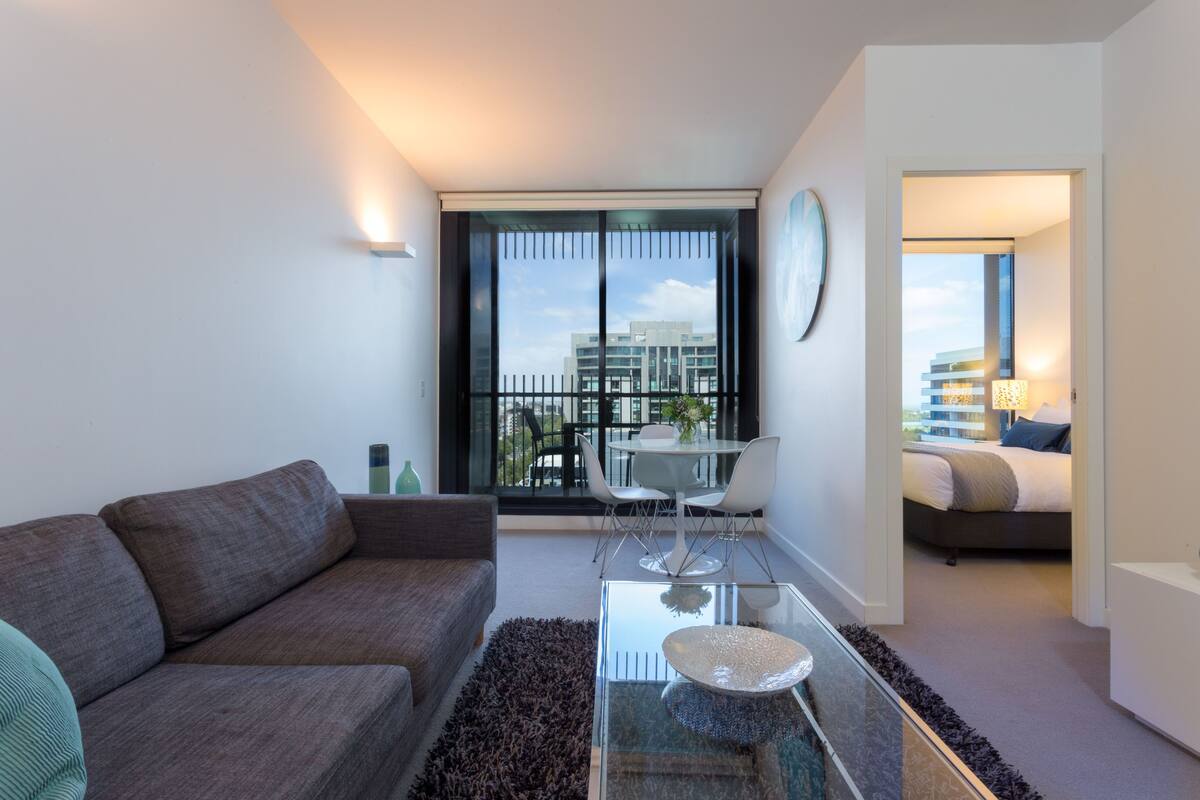 A modern living room with a sofa, a glass coffee table, and a dining area with chairs and a table.