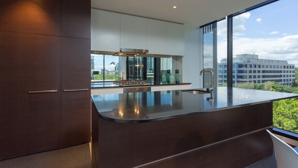 Een moderne keuken met donkere kastjes, een groot eiland en uitzicht op de skyline door grote ramen.