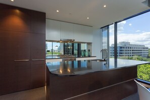 Een moderne keuken met donkere kastjes, een groot eiland en uitzicht op de skyline door grote ramen.