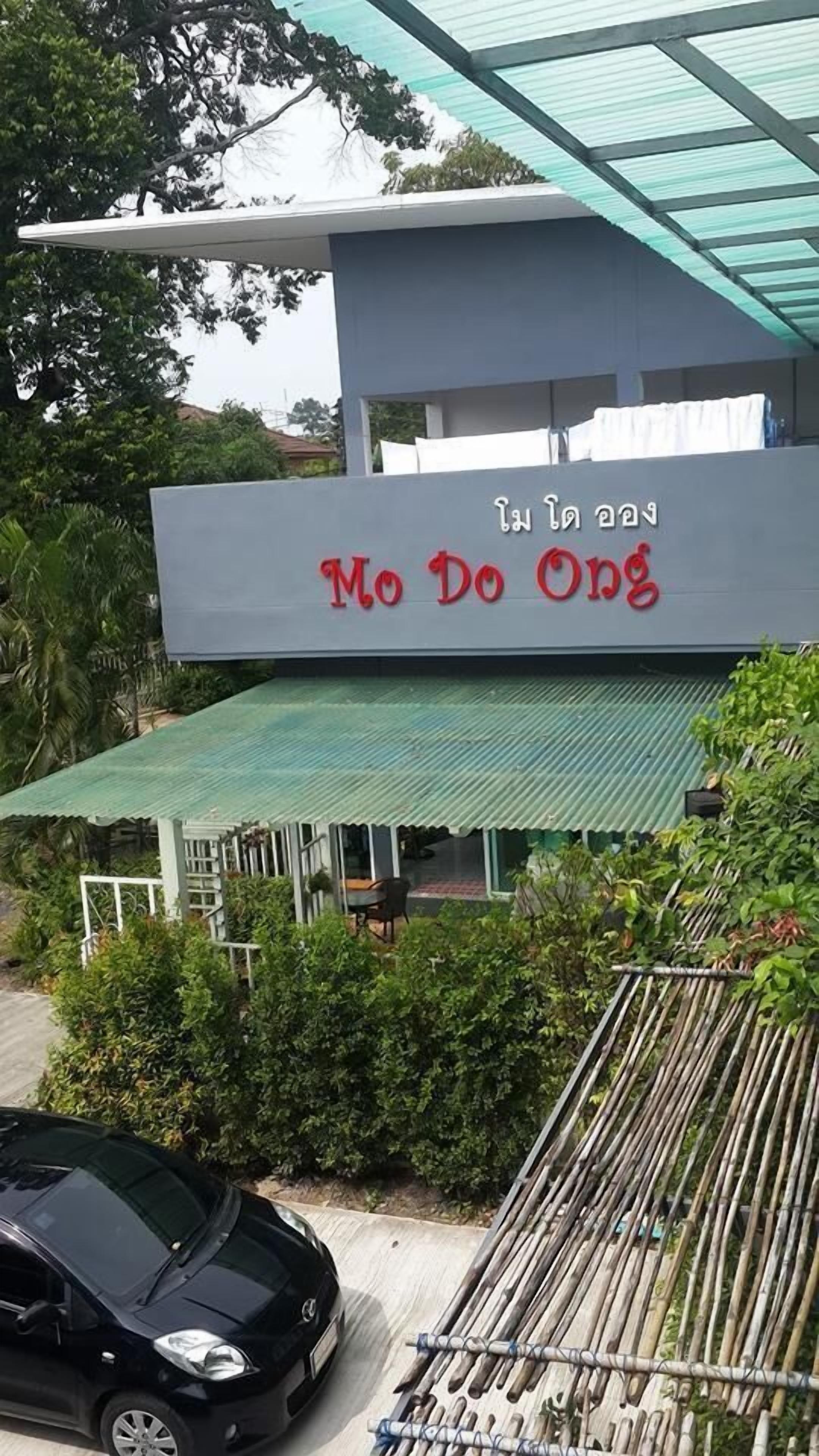 A building with a sign that reads "Mo Do Ong" and a covered outdoor area with a car parked in front.