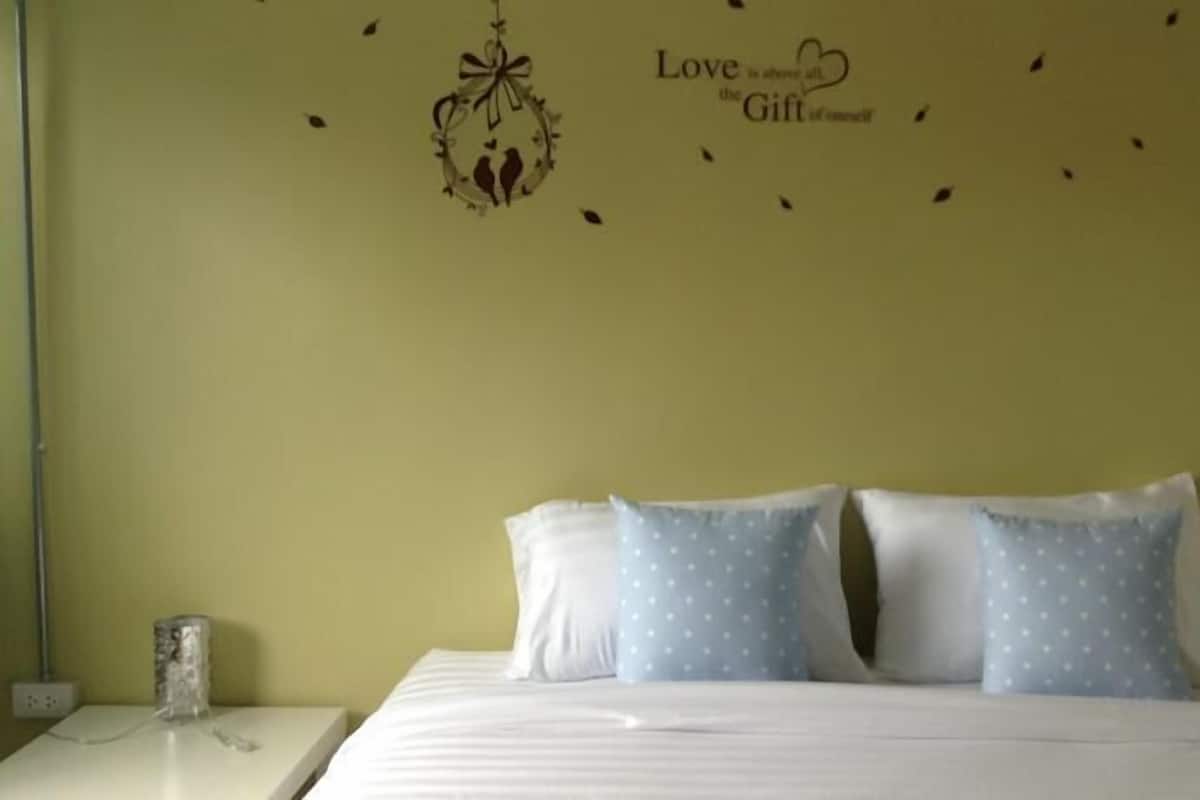 Un dormitorio con cama, dos almohadas, una mesita de noche y un adorno en la pared.