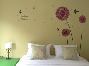 A bedroom with a bed, pillows, a nightstand, a lamp, and wall decorations including flowers and butterflies.
