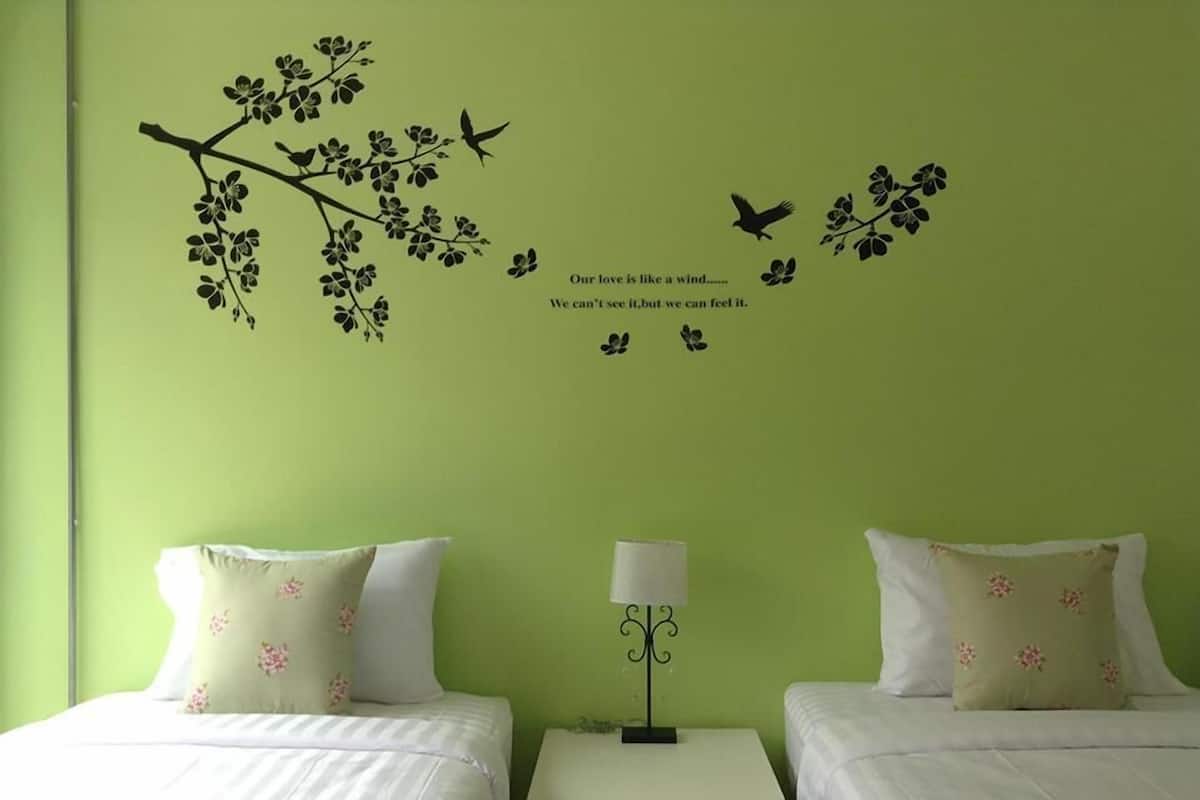 Habitación con dos camas, cada una con almohadas florales, una mesita de noche con lámpara y adhesivos murales de pájaros y flores.