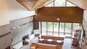 A spacious lobby with a high ceiling, a seating area with sofas and tables, a reception desk, and a large window providing natural light. - Inuyama International Youth Hostel (Inuyama)